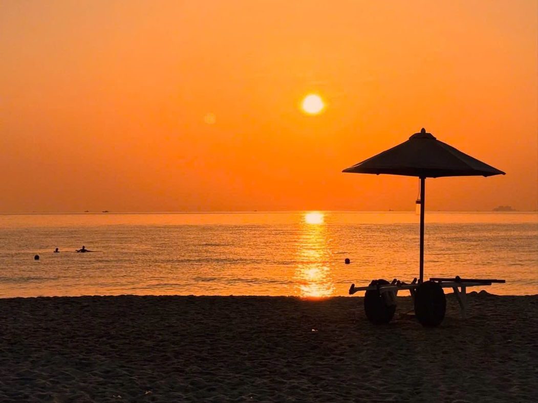 A single beach umbrella on the sand as the sun rises over a calm sea
