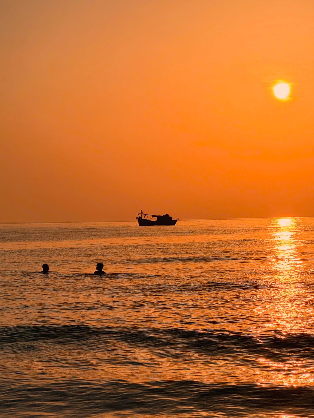 A fishing boat and two swimmers in an orange sunrise sea