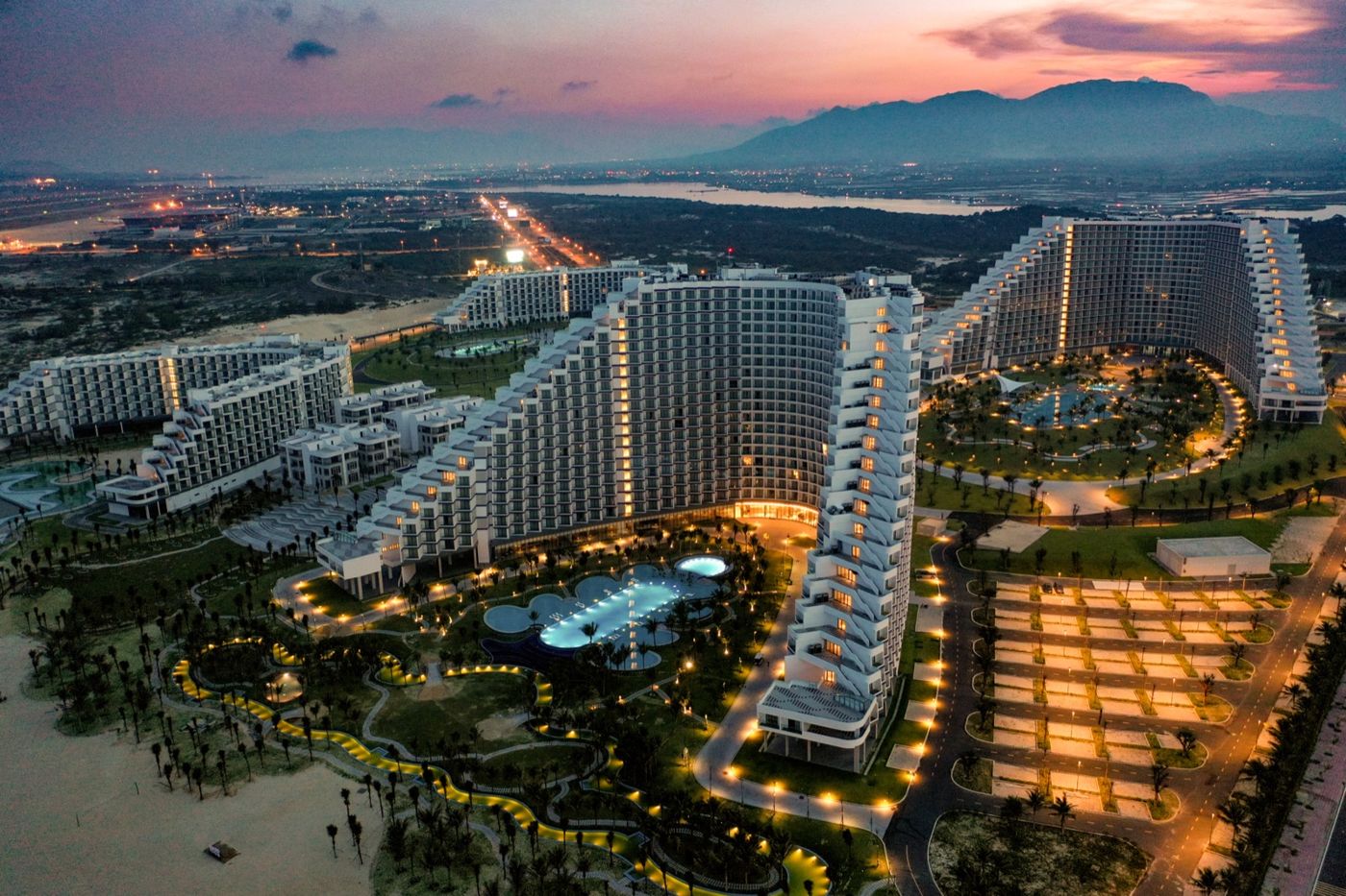 The resort lighting up at dusk under a pink sky over the hills